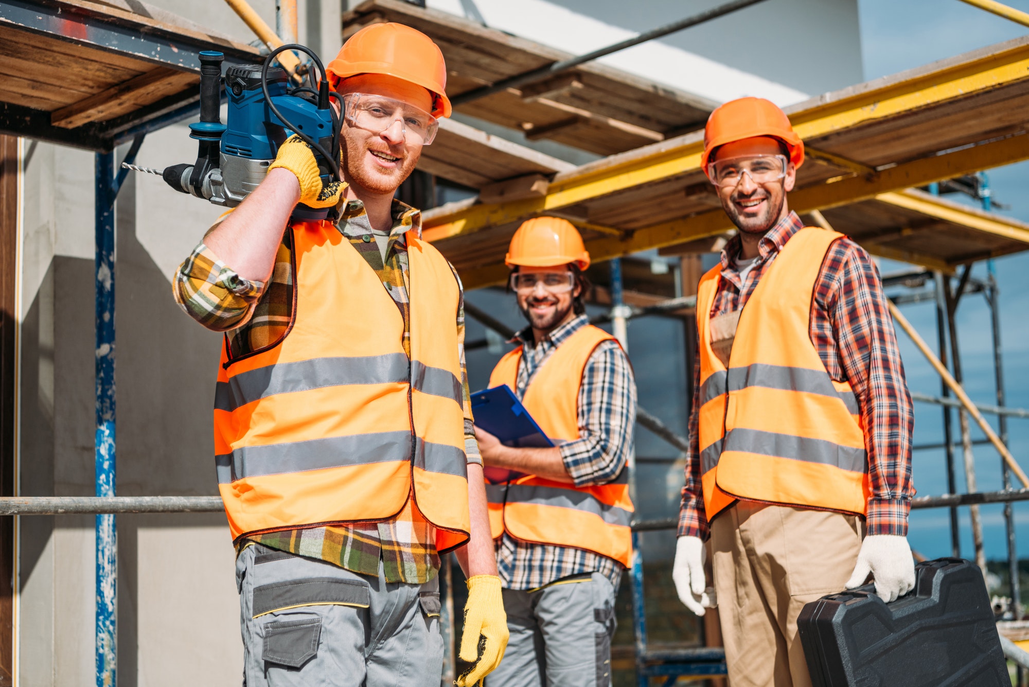 group of smiling builders with building equipment standing at construction site and looking at
